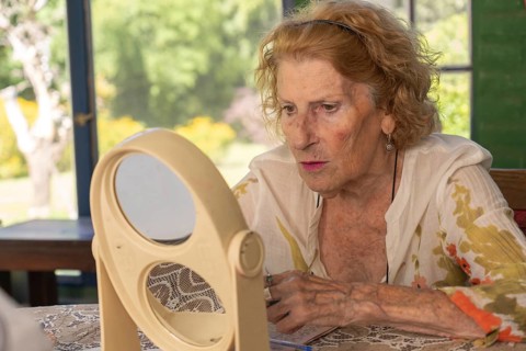 Senior woman applying makeup while gazing at her reflection in a double mirror on a table,