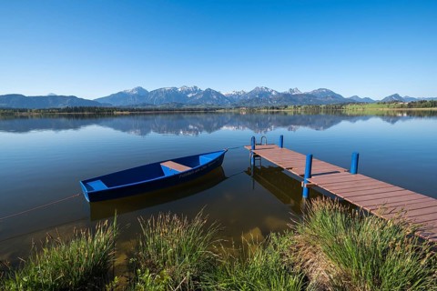 A blue jetty on a calm, clear lake with a breathtaking Alpine backdrop, Hopfen am See, near Füssen,
