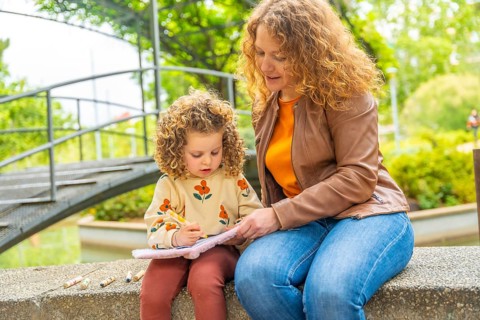 Blonde caucasian little girl learning to read on a park sitting with her mother
