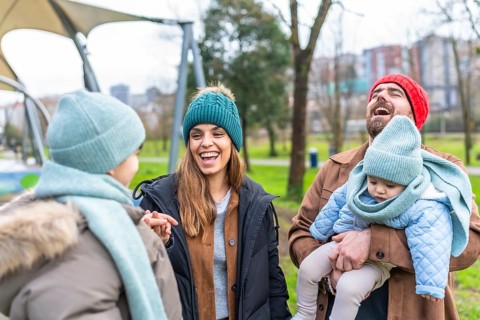 Happy parents holding their baby, laughing and talking with their other child in a park during