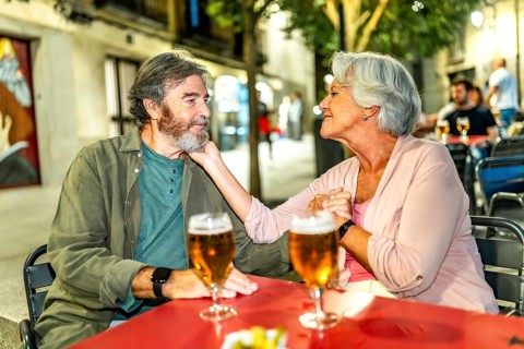 Senior woman caressing the face of her husband sitting on an outdoor terrace drinking beer at bar