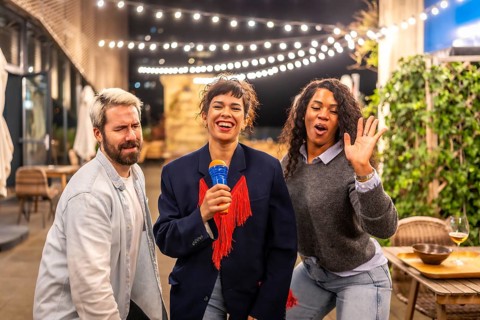 Happy diverse friends dancing and singing karaoke at night party in the roof terrace of an urban