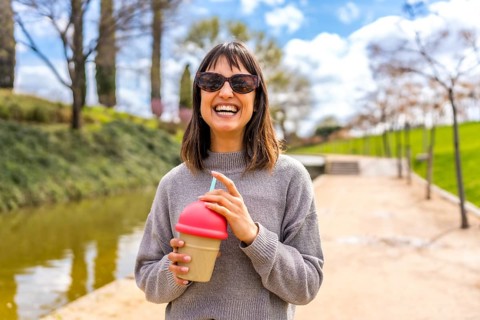 Young woman smiling and holding a reusable cup with a straw, enjoying a refreshing drink in a sunny