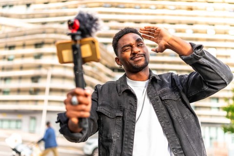 African man vlogger gesturing and winking while streaming online in the city