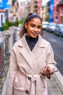 Vertical portrait of an elegant african american woman in tench coat using phone in the city