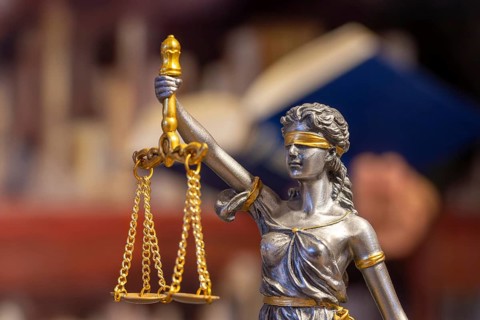 Close-up of a Justitia, in the background a man is reading a book (symbolic image)