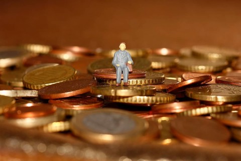 Miniature man sitting among euro coins, North Rhine-Westphalia, Germany, Europe