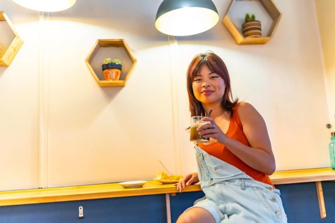 Low angle view portrait of an asian cool young woman smiling at camera sitting drinking coffee in a