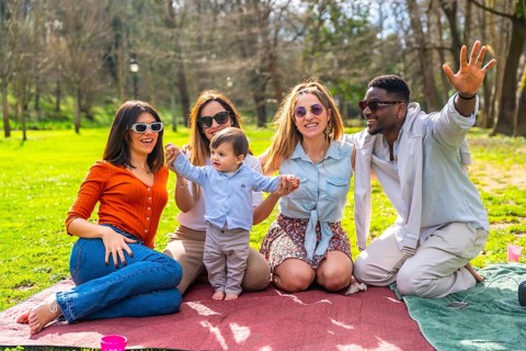 Group of cheerful multi ethnic friends with sunglasses enjoying picnic in a park with a baby boy