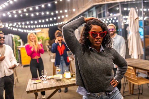 Sensual latin woman with sunglasses and casual winter clothes dancing next to friends at night