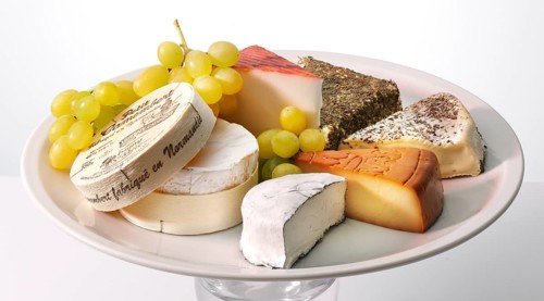 Cheese platter with various cheeses, decorated with grapes, studio shot