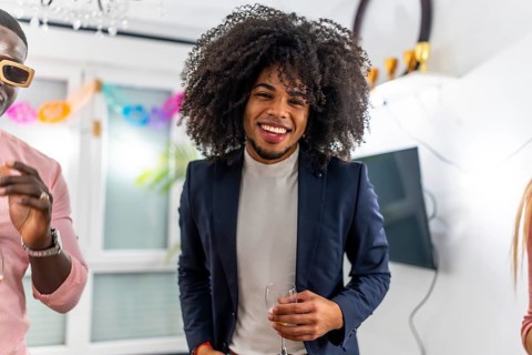 Latin cheerful man with curly hair smiling at camera during home party with friends