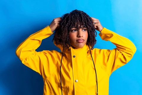 Young woman with curly hair wearing a yellow raincoat adjusting the hood while looking away on a