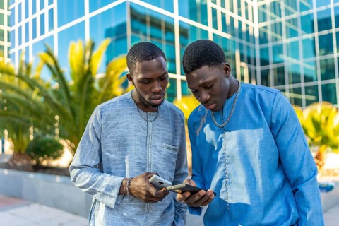 Two senegalese businessmen wearing traditional dashiki attire are using smartphones in front of a