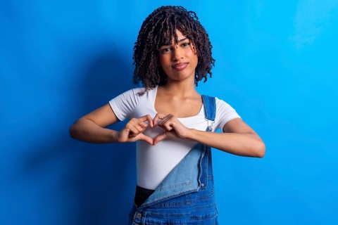 Studio portrait featuring a young woman forming a heart shape with her hands, radiating love and