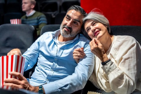 Senior couple enjoying a cozy movie night at the cinema, savoring popcorn while sharing a heartfelt