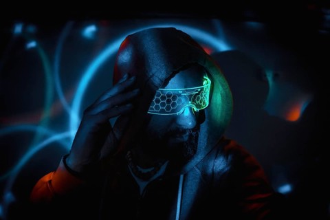 Bearded hacker adjusting futuristic glasses and touching his head in dark room with light effects