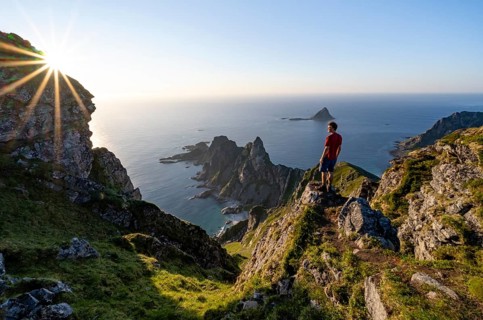 Mountaineer on the summit of Måtind or Måtinden, view of picturesque coastal landscape with sun
