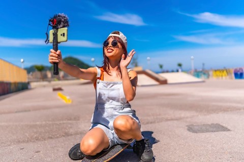 Asian young woman are doing livestreaming joyfully in skateboard urban park waving at the camera