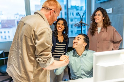 Business team congratulating their colleague on a successful project, shaking hands in the office