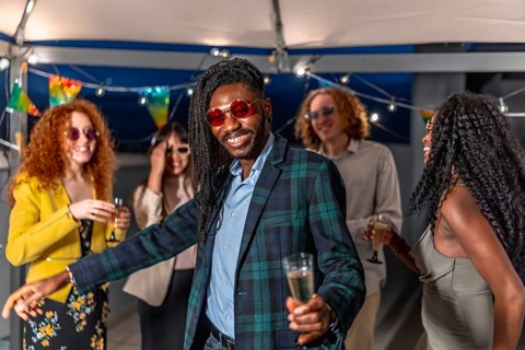 Portrait of a happy young african stylish man dancing with friends at night roof party
