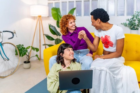 Transgender person and lesbian couple having fun using laptop together at home