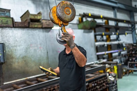 Mature caucasian man holding the hook of an industrial crane while operating in a factory