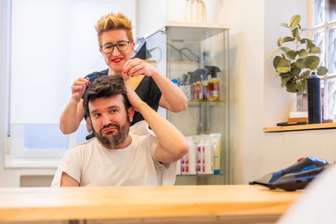 Reflection on the mirror of a modern hairdresser and satisfied man with new capillary prosthesis in
