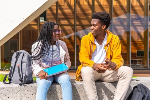 Two young African american students chatting relaxed outside the university sitting together under