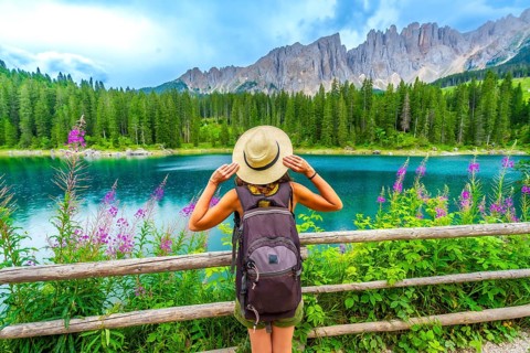 Female hiker with backpack admiring the turquoise waters of lake carezza and the latemar mountain