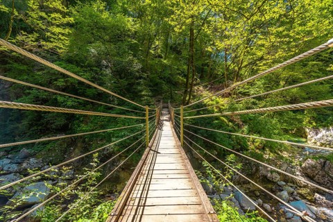 Wooden suspension bridge crossing over a clear stream in tolmin gorge, slovenia, surrounded by lush