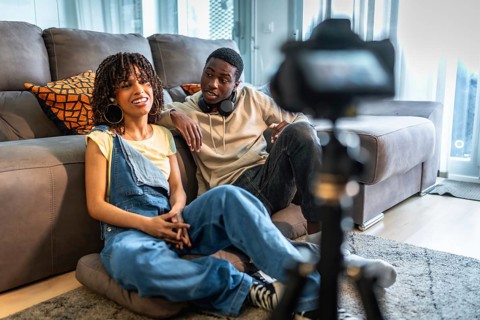 Two influencers are recording a vlog in their living room, discussing lifestyle and fashion tips