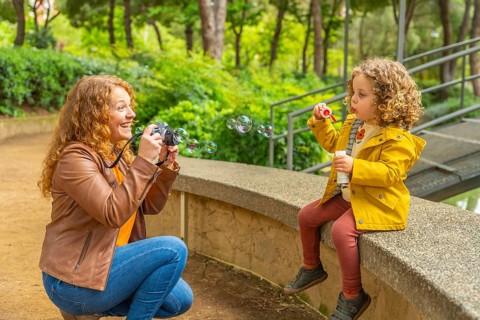 Mother taking portraits to her daughter blowing bubbles sitting on a park