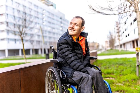 Young man using wheelchair smiling while enjoying a day out in an urban park, promoting inclusion