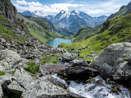 Hiker at the mountain stream and mountain lake Lac de Louvie with glaciated summit of the Grand