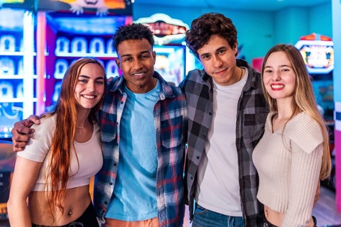 Four young multiethnic friends are smiling and having fun at an arcade, enjoying the weekend