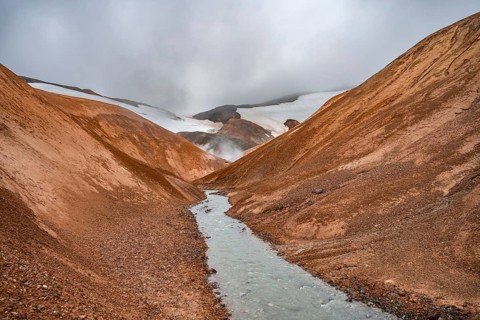 Steaming stream between colourful rhyolite mountains and snowfields, Hveradalir geothermal area,