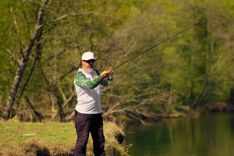 Man fish with spinning on river bank, casting lure. Outdoor weekend activity. Photo with shallow