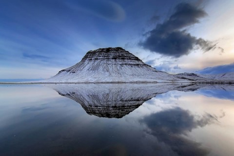 Kirkjufell, nunatak hill covered in snow reflected in water of fjord on the Snæfellsnes peninsula