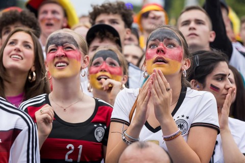 Women wearing make-up in the German national colours watch the football match in the fan zone at