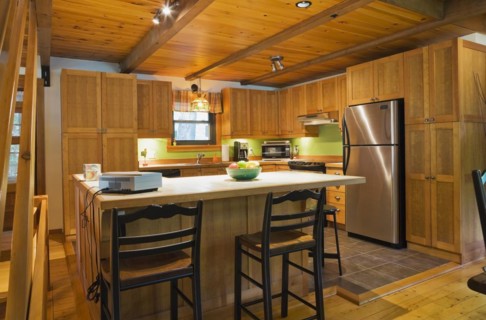 Wooden island with ceramic tile countertop, bar stools and shaker style cabinets in kitchen with