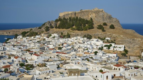 Clear daytime view of a coastal town with traditional Mediterranean architecture under a fortress,