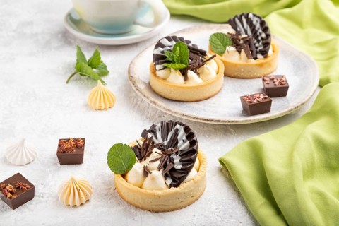 Sweet tartlets with chocolate and cheese cream with cup of coffee on a gray concrete background and