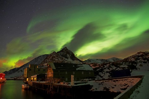 Night scene of a small village on the water, illuminated by auroras and lights from houses,