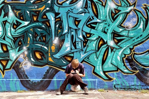 Ten-year-old boy playing with his Nintendo in front of a graffiti wall, football pitch, Germany,