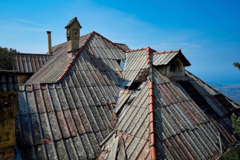 Dilapidated roofs of an old building with red tiles and a chimney under a clear blue sky, Mussolini