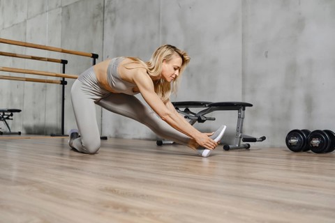 Fitness woman bends forward stretching the muscles of her back and legs in gym