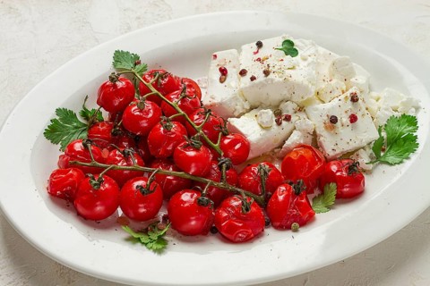 Baked cherry tomatoes, with cheese, and spices, on a white plate, homemade, no people