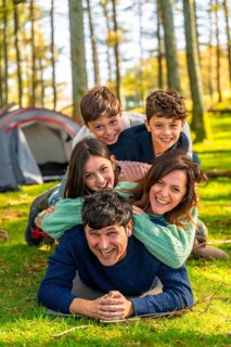 Vertical photo of a caucasian cheerful family laughing while lying down together at forest next to