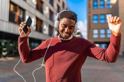 Happy african man listening to music with mobile and headphones dancing in the city street